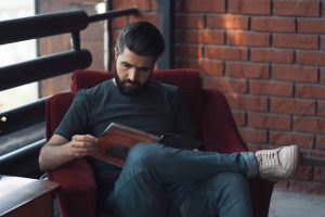 Portrait handsome bearded man wearing casual clothing. Man sitting in red chair modern loft studio, reading comics and relaxing