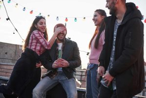 Young couple having fun with friends on the rooftop. Girl covers guy's face.